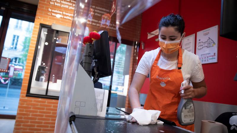 An employee wearing a protective mask and gloves cleans a checkout belt at a supermarket.