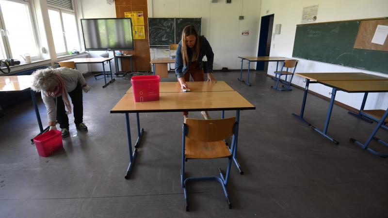 Teachers clean and disinfect chairs and tables at an empty school.