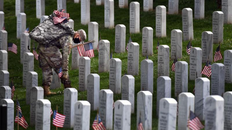 Member of military places flag near Arlington Cemetery headstone on May 21, 2020