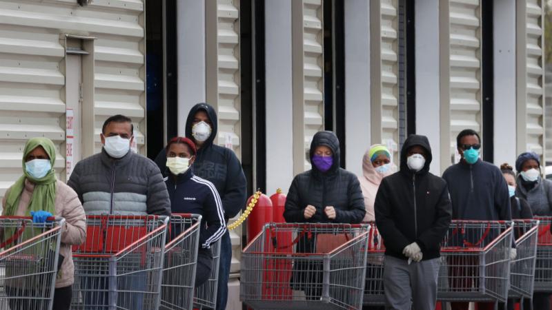 Shoppers wait in line while wearing masks