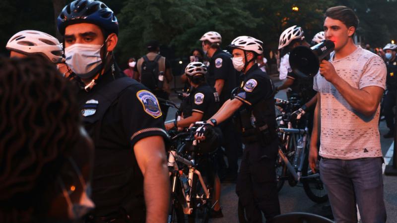 Police officers surround Jacob Wohl as he confronts protesters during a "Trump/Pence Out Now" rally in Washington, DC