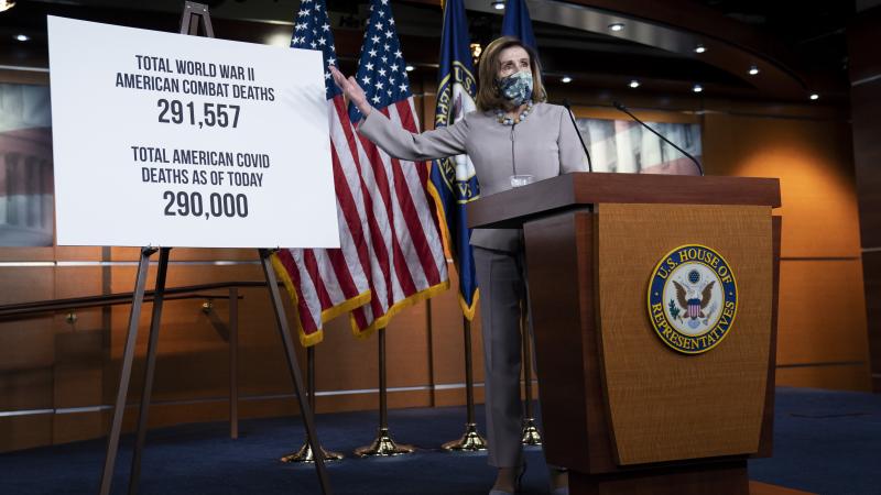 Speaker of the House Nancy Pelosi gestures to a sign listing the American COVID-19 death toll during her weekly news conference on Capitol Hill December 10, 2020 in Washington, DC.