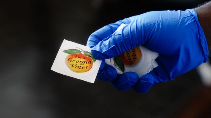 Polling place worker holding sticker to hand to a voter on June 9, 2020 in Atlanta, Georgia