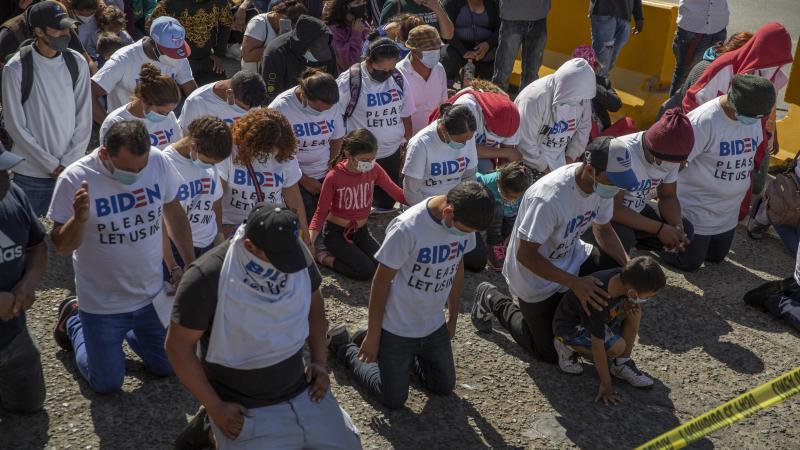 A group of migrants wearing T-shirts that read "Biden, please let us in" kneel and pray at the border crossing. The group gathered and marched up to the border post to petition the new U.S. administration for asylum.