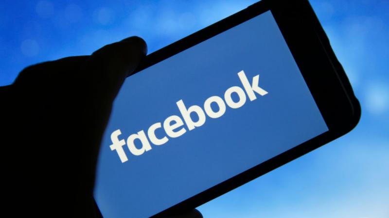 Facebook logo seen on screen of iPhone in photo illustration