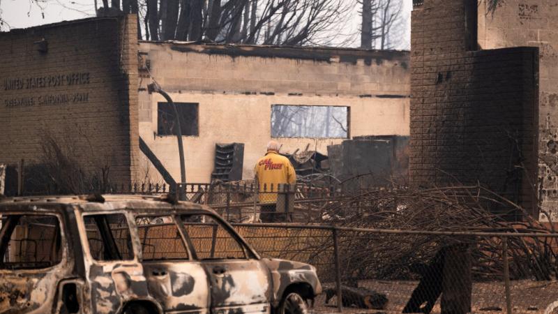A CalFire personnel inspects the remains of a burned U.S. Post Office destroyed by the Dixie Fire 