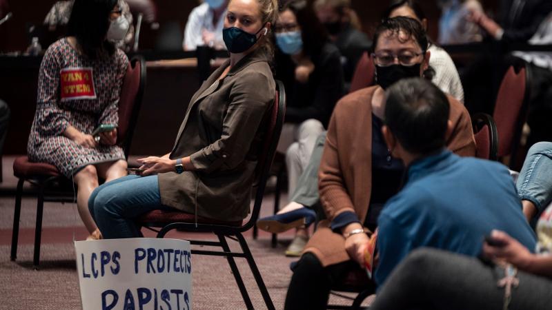 A woman sits with her sign during a Loudoun County Public Schools (LCPS) board meeting in Ashburn, Virginia on October 12, 2021.