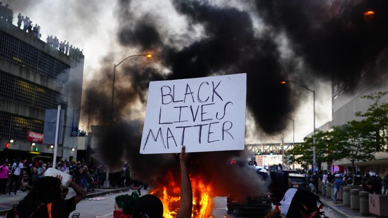 Man holds Black Lives Matter sign as police car burns during protest, Atlanta, May 29, 2020
