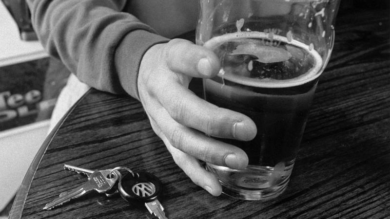 A man holding a pint of lager with his car keys next to it on a table