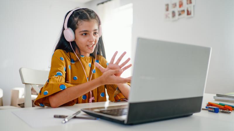 Teenage girl with headphones and laptop having online school class at home