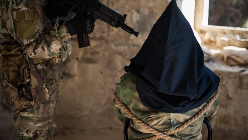 A masked prisoner is held at gunpoint