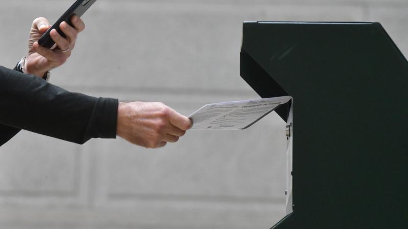 A man photographs himself depositing his ballot in an official ballot drop box while a long line of voters queue outside of Philadelphia City Hall at the satellite polling station on October 27, 2020 in Philadelphia, Pennsylvania.