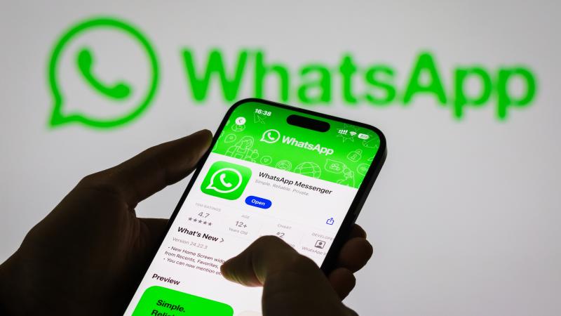 A person holds a smartphone displaying the WhatsApp app page, with the WhatsApp logo in the background, on November 6, 2024 in Chongqing, China.