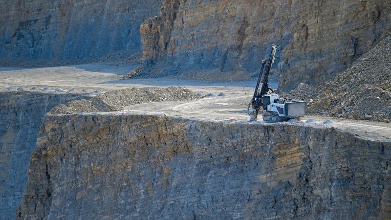 Driller blasts holes on limestone cliff.