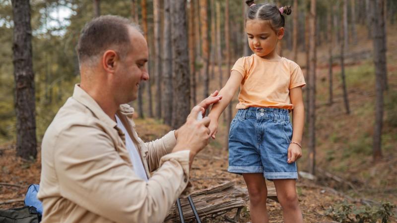 Father sprays tick repellent on daughter in forest.