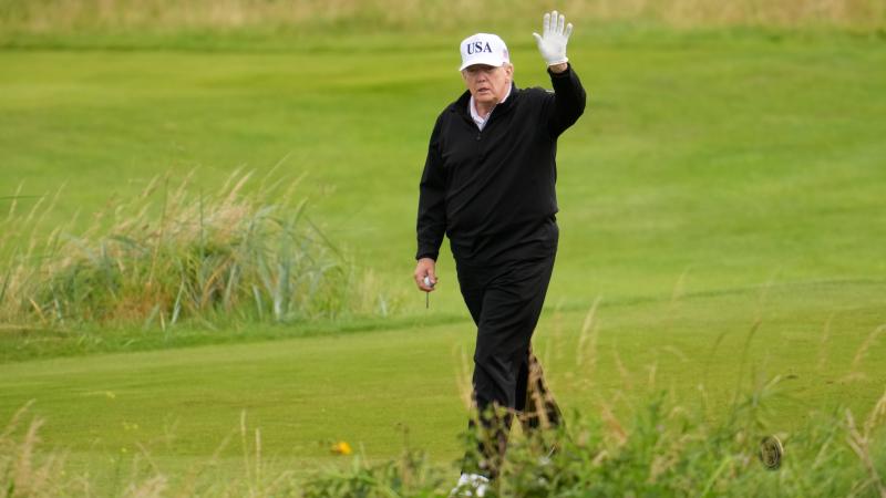 Trump waves while walking through golf course in Scotland.