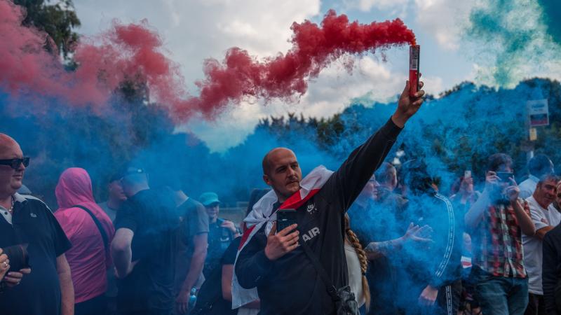 A man holds a flare during a protest outside The Bell Hotel on July 31, 2025 in Epping, England. Anti-migrant protesters, as well as counter-protesters, have organised rallies in Epping near the Bell Hotel, which is being used as migrant accommodation.