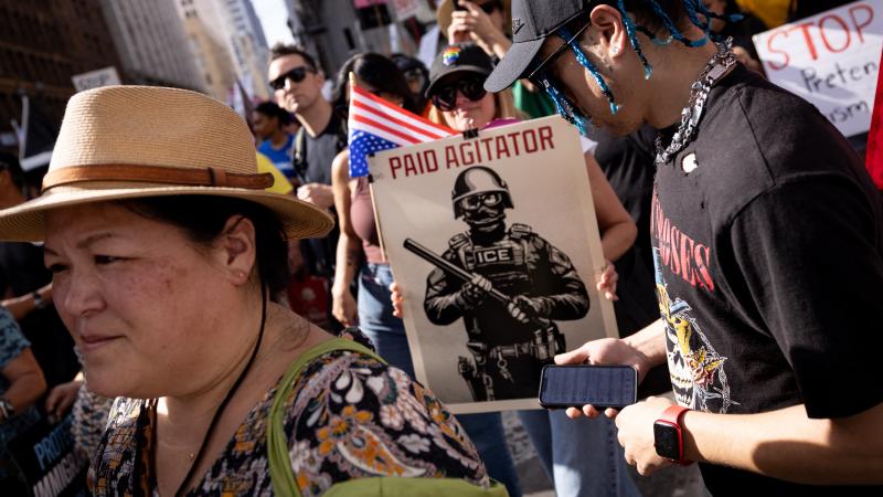 Demonstrators hold a sign depicting an ICE agent as a paid agitator during the "No Kings" national day of protest in Los Angeles on March 28, 2026