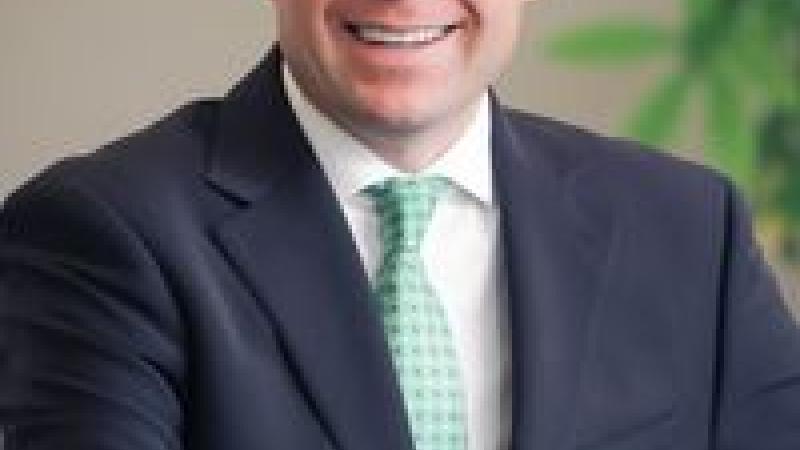 GOP candidate Reid Rasner sits at a desk in a blue suit and green tie