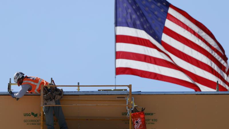 An American flag flies near a construction worker during construction of a new building on March 6, 2026 