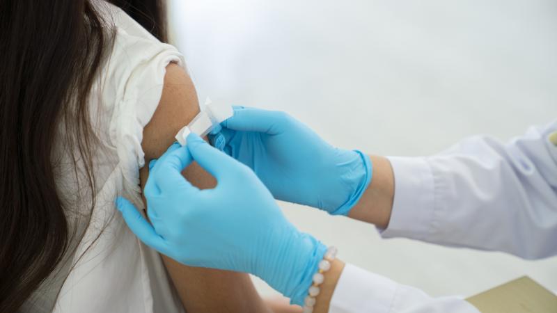 Doctor applies bandage to preteen girl's arm following an immunization