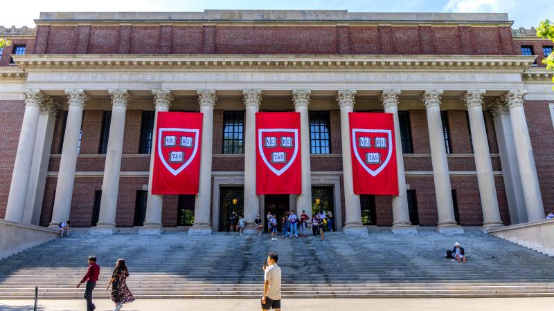 Crowd of visitors in front of the Harry Elkins Widener Memorial Library (c. 1915). Harvard VERITAS shield banners hang in front of the building. The library houses some 3.5 million books in its stacks and is the center­piece of the Harvard College Libraries. It honors 1907 Harvard College graduate and book collector Harry Elkins Widener.