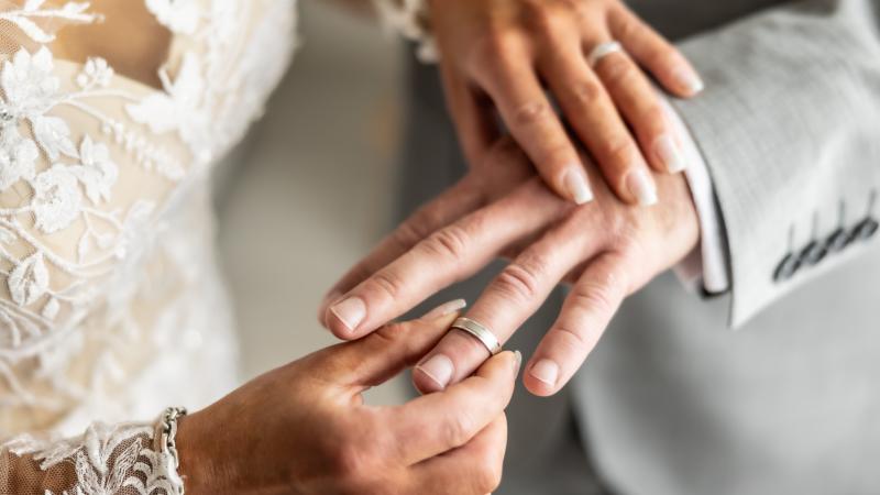 Wedding rings exchange with bride putting a ring on her future husband's finger. - stock photo