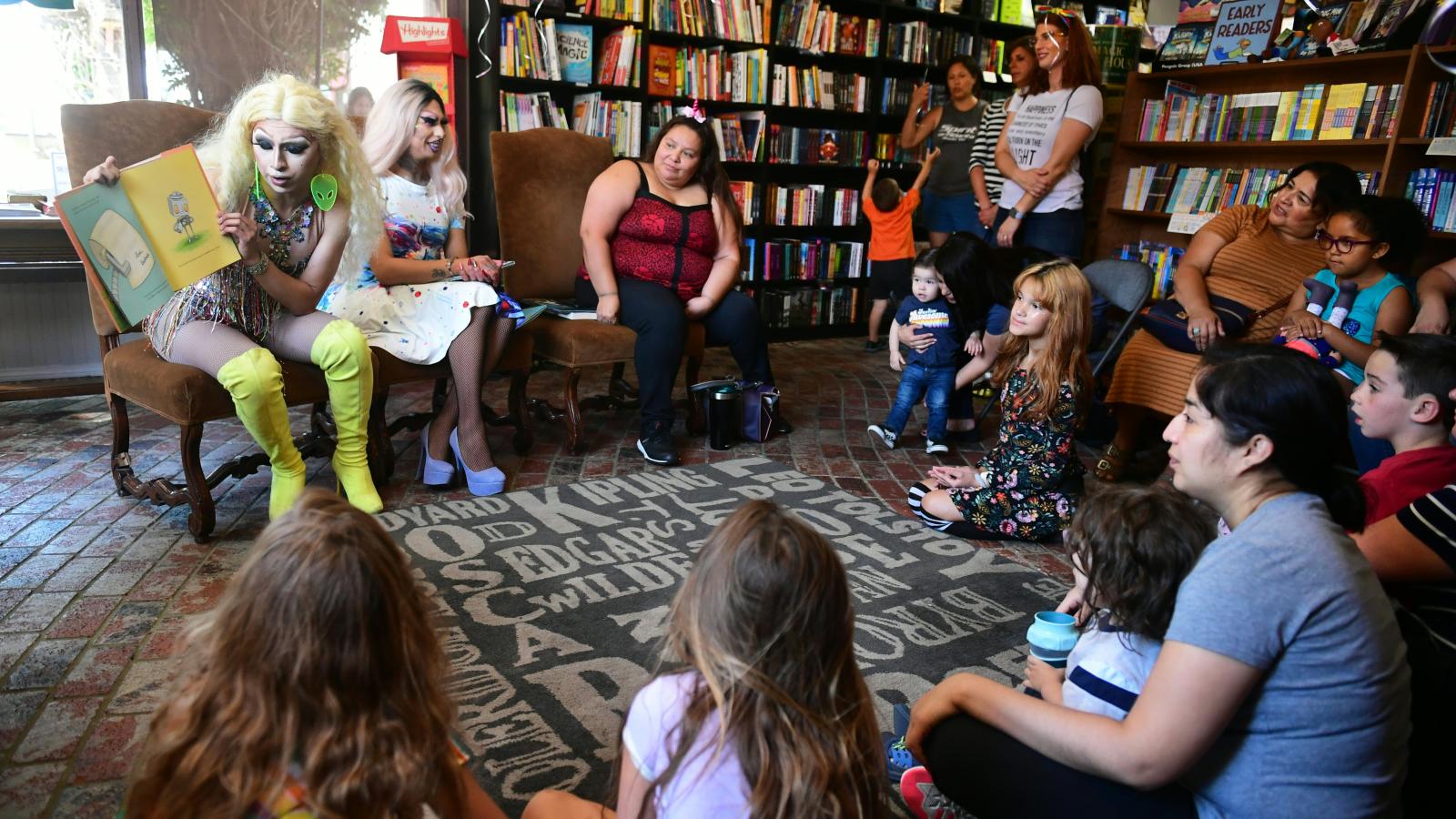 Drag queen Athena Kills (L) reads seated beside Scalene Onixxx to adults and children during Drag Queen Story Hour at Cellar Door Books in Riverside, California on June 22, 2019.