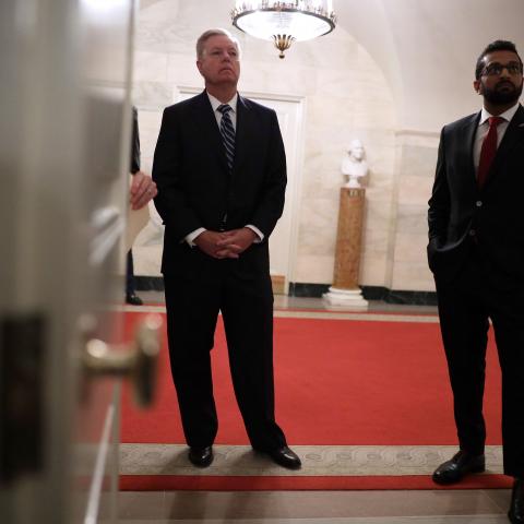 U.S. Sen. Lindsey Graham (R-SC) (L) and National Security Council Senior Director of Counterterrorism Kashyap "Kash" Pramod Patel listen as U.S. President Donald Trump makes a statement in the Diplomatic Reception Room of the White House October 27, 2019 in Washington, DC.